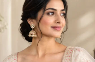 Indian woman wearing traditional gold-toned jhumka earrings with pearl detailing, styled with an elegant embroidered outfit.